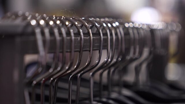 Clothing hangers macro close-up video of empty metal clothes hangers aligned on a rack. Shallow depth of field, retail store atmosphere, minimalist fashion and shopping concept.