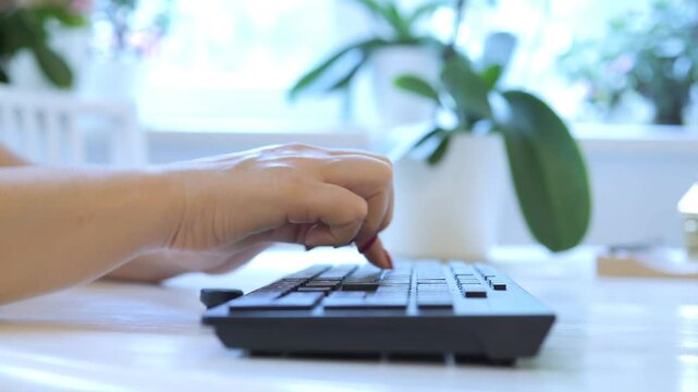 Woman is typing on a keyboard. The keyboard is black and has a white space bar. The woman is wearing red nail polish