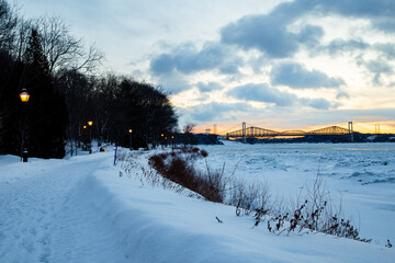Fototapeta premium Winter panorama with the Jacques-Cartier walk along the frozen St. Lawrence River, with the 1970 Pierre-Laporte and the 1904 Quebec bridges in the background, Quebec City, Quebec, Canada