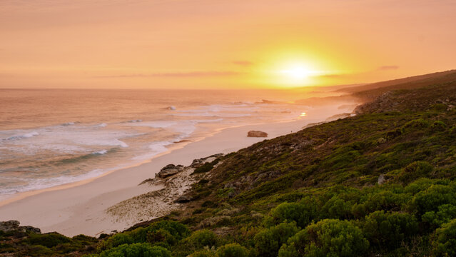 Experience the magical hues of a sunset illuminating the tranquil beaches near Hermanus. This picturesque scene along the Garden Route captures the essence of South Africa natural beauty.