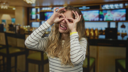 Woman holds her hands while smiling inside a cafe where a blonde young guest makes a playful...