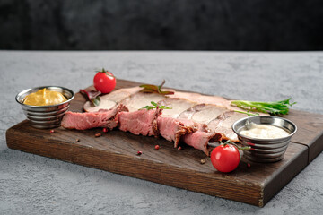 Thinly sliced rare roast beef and tender pork served with creamy horseradish, Dijon mustard, tomatoes and arugula on wooden cutting board. Premium cold cuts assortment, sophisticated meat dish