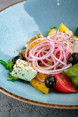 Classic Greek salad with feta cheese cubes, black olives, cherry tomatoes, cucumber, red onion rings, bell pepper and fresh greens in blue bowl. Vibrant Mediterranean appetizer, healthy gourmet dish