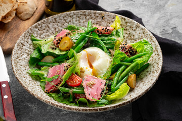 Fresh seared tuna salad with poached egg, green beans, potatoes, tomatoes and sesame seeds. Healthy gourmet meal, nutritious food photography on rustic plate, close up