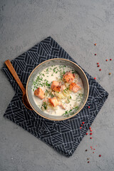 Creamy potato soup topped with seared salmon pieces and chopped herbs in ceramic bowl. Rich Nordic salmon chowder, wholesome seafood meal, top view