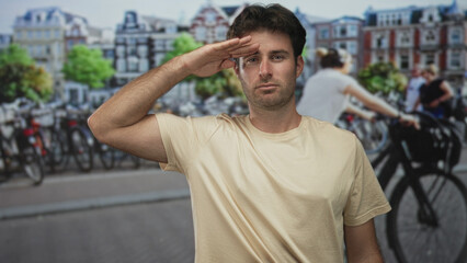 Fototapeta premium Young man salutes with hand to forehead on amsterdam street beside rows of parked bicycles; respect duty.