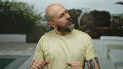 Fototapeta premium Bald man with beard relaxing outdoors near pool in resort hotel showcasing serene and peaceful vacation vibes