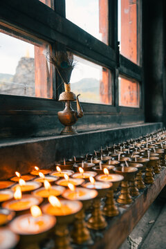 View of rows of flickering butter lamps casting a warm glow against the dark window frame, with a glimpse of mountains in Jambay Lhakhang, Jakar, Bhutan.