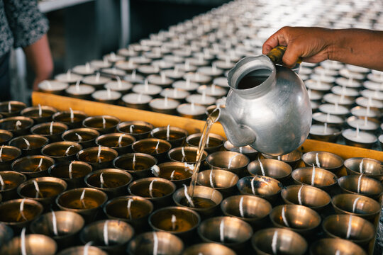 View of golden light reflecting off the water being poured from a silver teapot into rows of brass offering bowls, Jambay Lhakhang, Jakar, Bumthang, Bhutan.