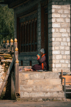 View of a monk in deep contemplation, clad in traditional robes, sits peacefully on the stone steps of a temple with intricate carvings, Jambay Lhakhang, Bumthang, Bhutan.