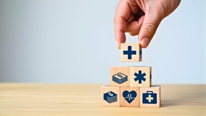 Hand places a medical cross block onto a stack of wooden cubes featuring diverse healthcare icons, illustrating comprehensive medical services and health insurance concepts
