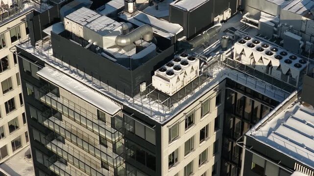 Drone footage shows a modern apartment building rooftop in winter, featuring snow-covered surfaces, ventilation ducts, HVAC units, and contemporary urban architecture.