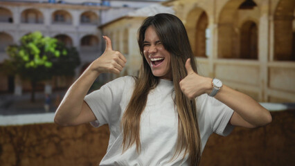 Woman smiling indoors at an old university setting with thumbs up and long hair, wearing a casual...