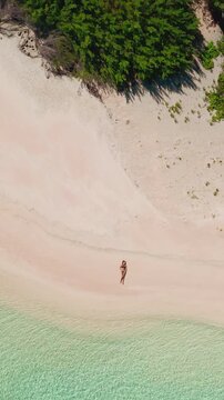 Woman enjoying a tranquil pink sand beach on a secluded tropical island in the maldives, with crystal-clear turquoise waters lapping at the shore