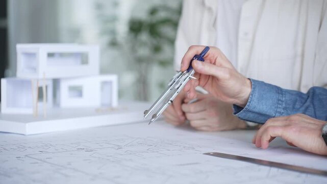 Architects collaborating on blueprint plans, discussing engineering details and project designs, planning construction development with a laptop in a modern office environment
