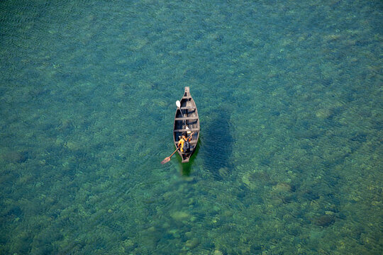 Shillong, India - 18 January 2019: View of a solitary boat glides on the Umngot River, its clear turquoise waters revealing the riverbed below, casting a serene spell.
