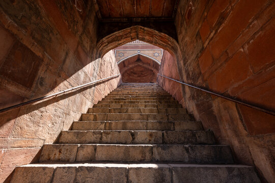 View of sandstone steps ascending towards an arched doorway, framed by rough-hewn walls and bathed in dappled light, Delhi, Delhi Division, India.