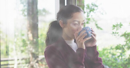 Fototapeta premium Holding blue ceramic mug, woman wearing maroon sweater sipping at home near dotted glass window