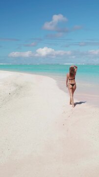 Young woman in bikini walking perfect white sand beach, blue sky, turquoise water. Slim caucasian female relax, enjoy outdoor lifestyle travel on summer holiday vacation, Maldives tropical island.