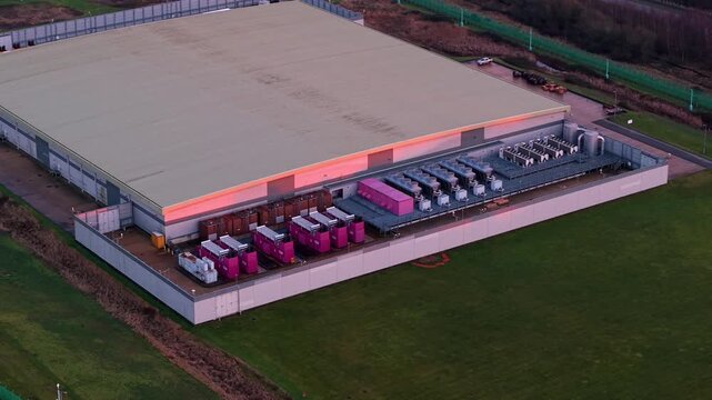 Aerial view of the Lloyds Horizon Data Centre, with its expansive roof and vibrant pink and grey equipment contrasting against the surrounding green landscape, Corby, United Kingdom.
