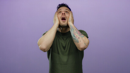 Young man with tattoo on purple background looks perplexed, expressing emotions using his hands, in...