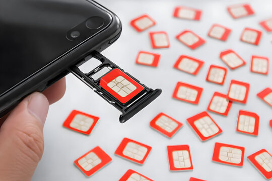 A hand holding a smartphone with a sim card tray and many sim cards scattered on a white surface