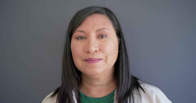 Woman seeing camera cue, opening eyes, meeting gaze in gray set, in green top, smiling, laughing