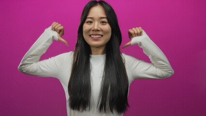 Fototapeta premium Woman smiling in front of a vibrant pink background wearing a white shirt with long dark hair and making gesture of pointing to herself while standing confidently.