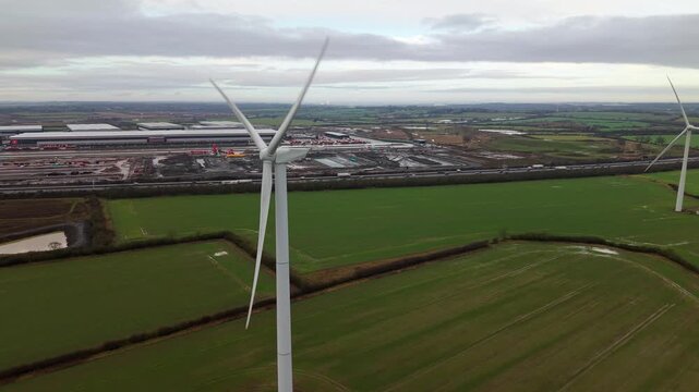 Aerial view of wind turbines standing tall amidst the lush green fields contrasting with the grey skies, Yelvertoft, Crick, United Kingdom.
