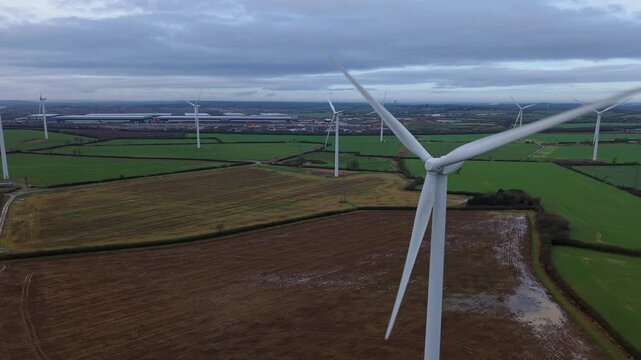 Aerial view of white wind turbines stand tall against the backdrop of green fields and a cloudy sky, creating a striking contrast, Yelvertoft, Crick, United Kingdom.