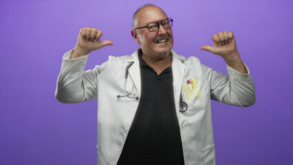 Naklejka premium Man doctor in white coat points thumbs to chest with stethoscope and glasses in studio; confidence warmth.