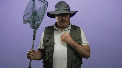 Senior hispanic man fisherman holding a landing net and pointing index finger upward while wearing...