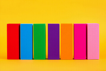 Seven colorful books lined up on a shelf in red blue green purple orange pink and light pink on a yellow background