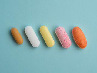 Various colorful pills and capsules on blue background, displaying various medicines, vitamins and supplements for healthcare and pharmacy concept.