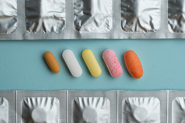 Various colorful pills and capsules on blue background, displaying various medicines, vitamins, syringe, stethoscope, supplements for healthcare and pharmacy concept.