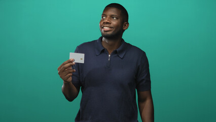 Man holding creditcard between fingers in studio, presenting a white card while smiling and looking aside; financial confidence.