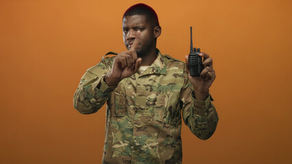 Man soldier holding radio and pointing finger in studio wearing camouflage uniform and alert stance; discipline authority duty.