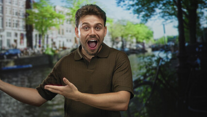 Fototapeta premium Man with open hands and open mouth gesturing on a canal street in amsterdam near bicycles and canal boats; joy travel discovery.