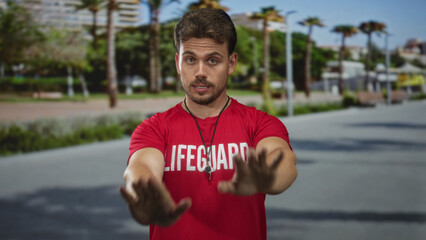 Fototapeta premium Man lifeguard in red shirt with whistle and outstretched palms stopping gesture on street; duty vigilant.