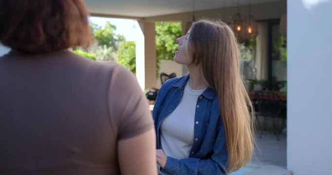 Two women, woman walking to doorway visiting neighbor, greeting at patio in denim shirt waist bag