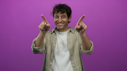 Hispanic man smiling in front of vibrant pink background, wearing casual plaid shirt and white t-shirt, radiating charm and confidence.