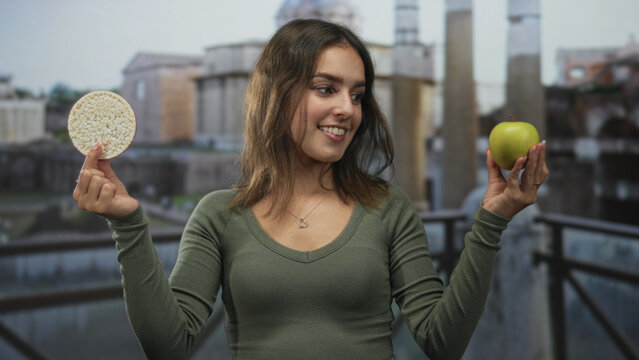 Woman smiling holding green apple and rice cake with hands in front of building; mindful eating wellness joy.