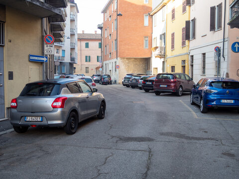 Suzuki Swift and Renault Clio cars parked on a narrow urban street in Italy, city architecture and residential buildings