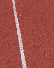 Red track surface shows white lane marking for running practice in sports field during daytime