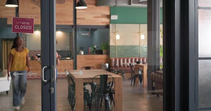 Two adult women walking toward glass doors, flipping closed sign to open cafe, pulling handles
