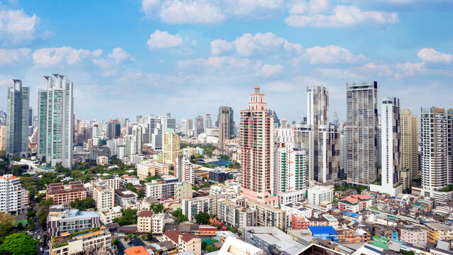 High angle view of Bangkok's skyline and urban landscape under a bright blue sky. The image shows a mix of modern skyscrapers and residential buildings in the central business district