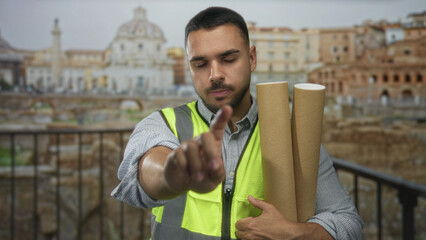 Man holds rolled blueprint under arm and raises palm in stop gesture at building overlooking...