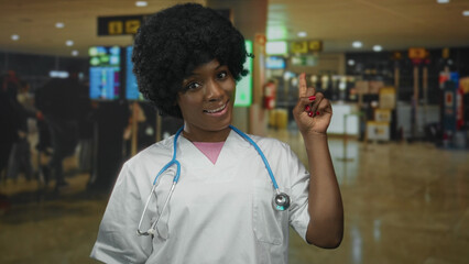 Woman wearing scrubs and stethoscope points finger at departure board in bustling airport;...