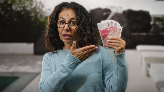Middle-aged woman holding icelandic krona banknotes on a city street, showcasing economy and finance concepts in an outdoor urban setting.