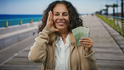 Woman holding romanian money by the seaside with a boat in the background, showcasing a middle aged...